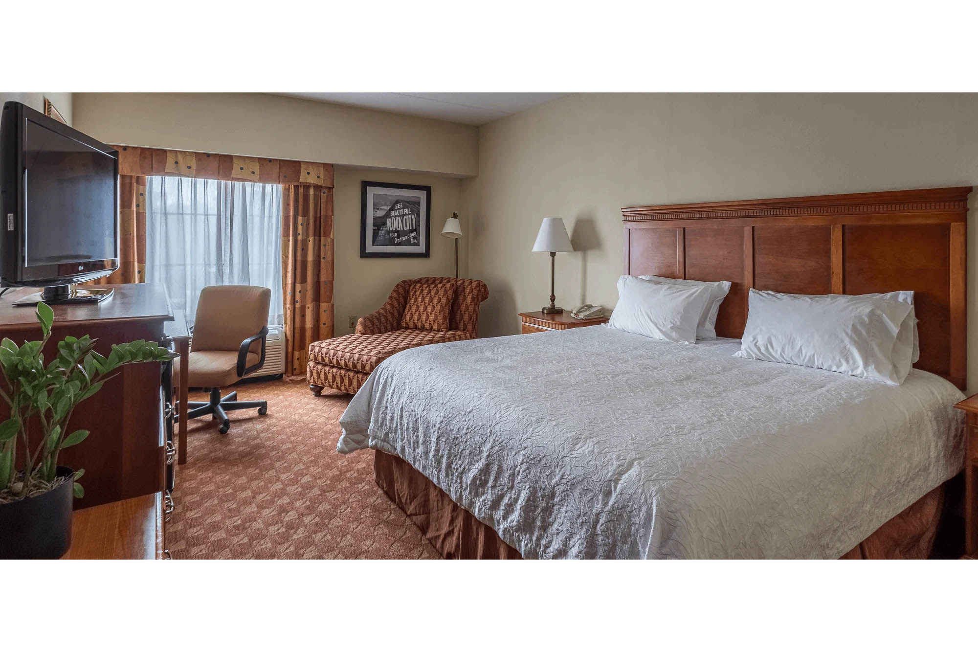 Tennessee interior photography of a hotel guest room featuring a king bed, seating area, desk, television, and natural window light