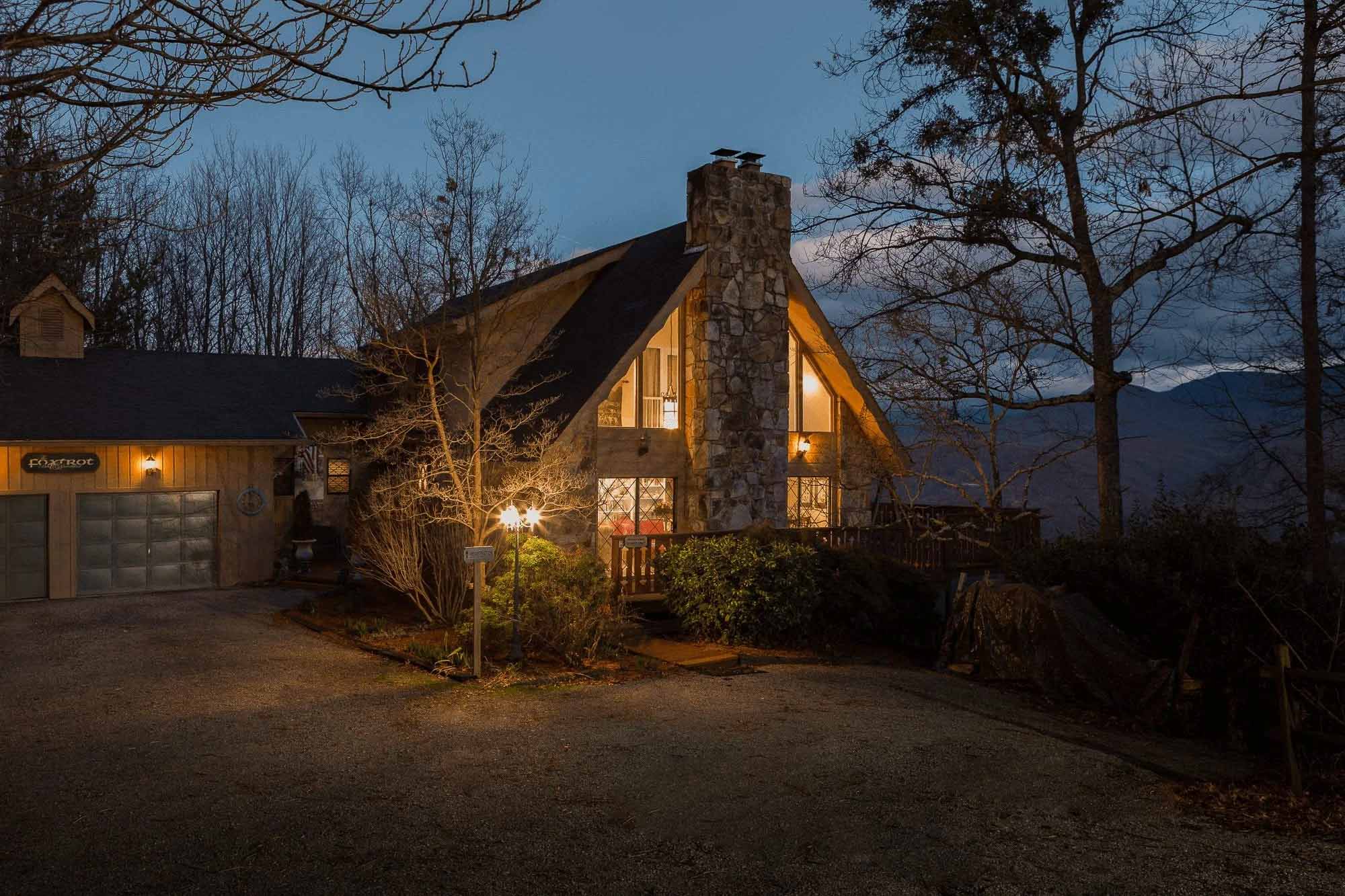 Gatlinburg architectural photography of a mountain cabin exterior at twilight featuring a stone chimney, warm interior lighting, and wooded surroundings